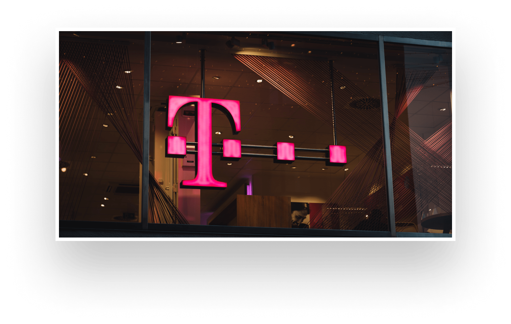 Ein leuchtendes Telekom Logo hängt an einer Glaswand.