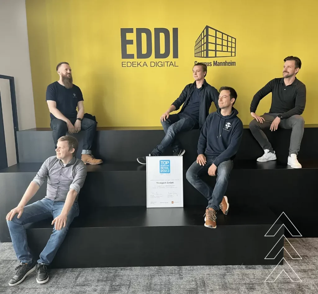 Vor der gelben Hintergrundwand mit dem Eddi Logo von Edeka sitzen im Dominik, Laszlo, Patrick, Thomas und Jens und die "Top Supplier" Urkunde.